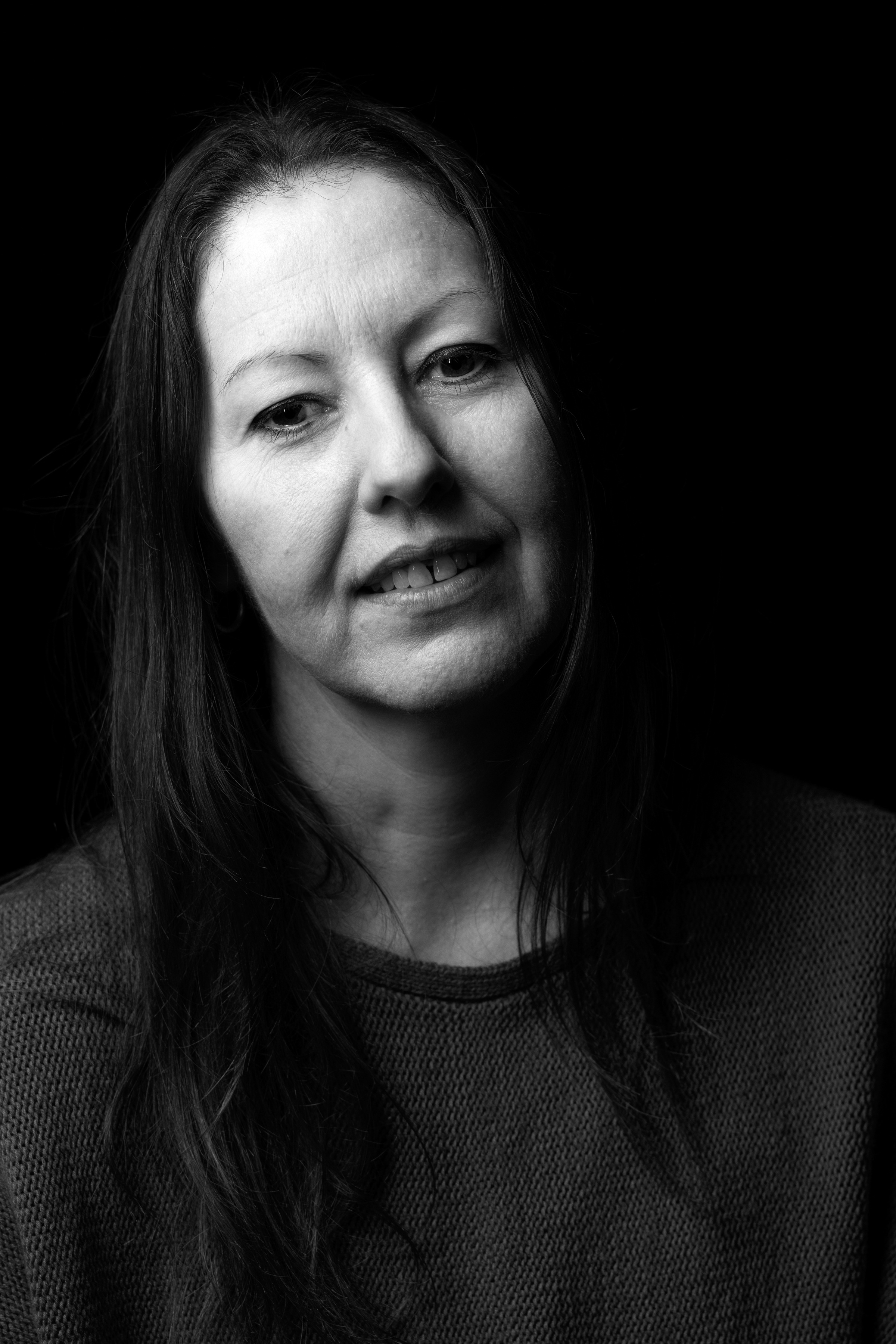 Grayscale portrait of a woman with long hair, smiling softly against a dark background.